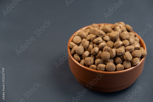 Bowl of dog food against a gray background. Round brown pellets in a ceramic bowl. Food for neutered and straitened pets. Healthy food. Angled view from above. Copy space for text and design elements photo
