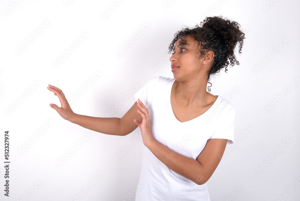 Displeased Young beautiful girl with afro hairstyle wearing white t-shirt over white wall keeps hands towards empty space and asks not come closer sees something unpleasant Displeased Young beautiful girl with afro hairstyle wearing white t-shirt over white wall keeps hands towards empty space and asks not come closer sees something unpleasant