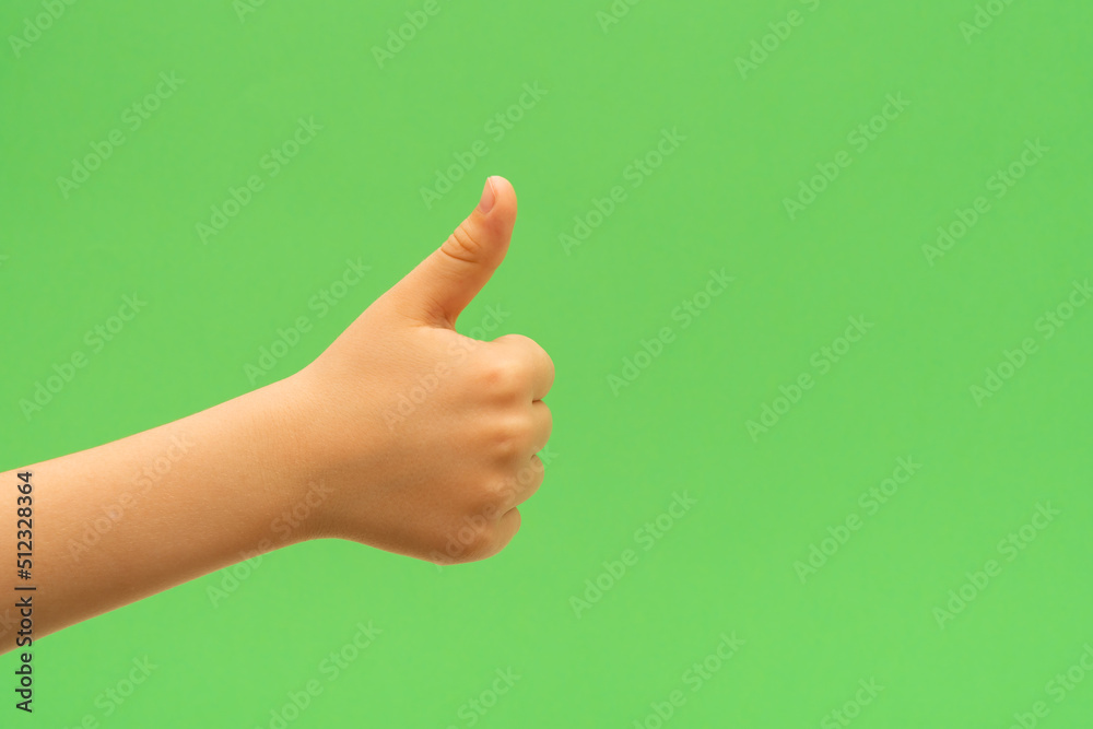 Child hand with enjoyment thumb up gesture on green background.