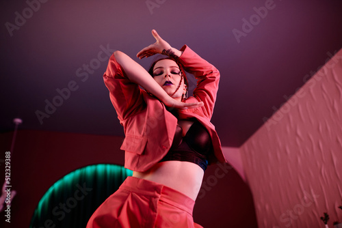 Low angle portrait of sensual young woman dancing vogue style in pink neon light with focus on hand movements photo