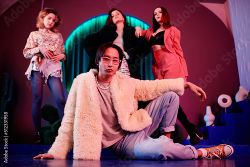 Full length portrait of club dance crew in red neon light with focus on extravagant male leader in foreground
