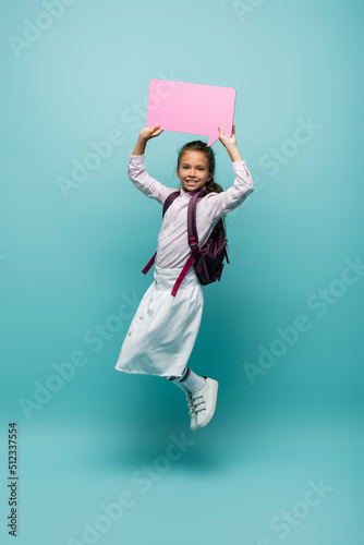 Positive pupil with backpack holding speech bubble on blue background.