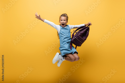 Excited schoolkid with backpack jumping on yellow background. photo