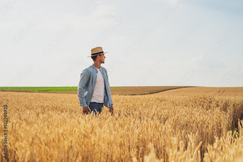 Happy farmer is standing in his growing wheat field.