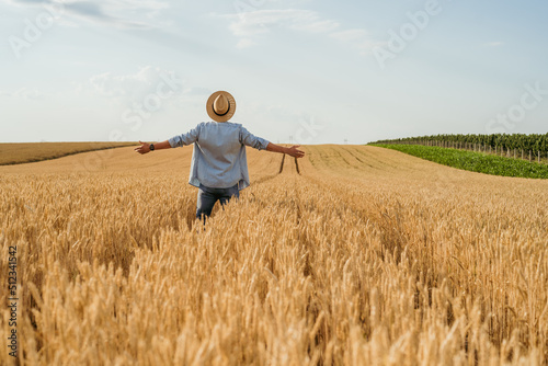 Happy farmer with arms outstretched standing in his growing wheat field. 