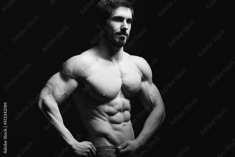 Portrait of shirtless muscular man in a jeans. Young male hunk showing his perfect body and muscles on black background