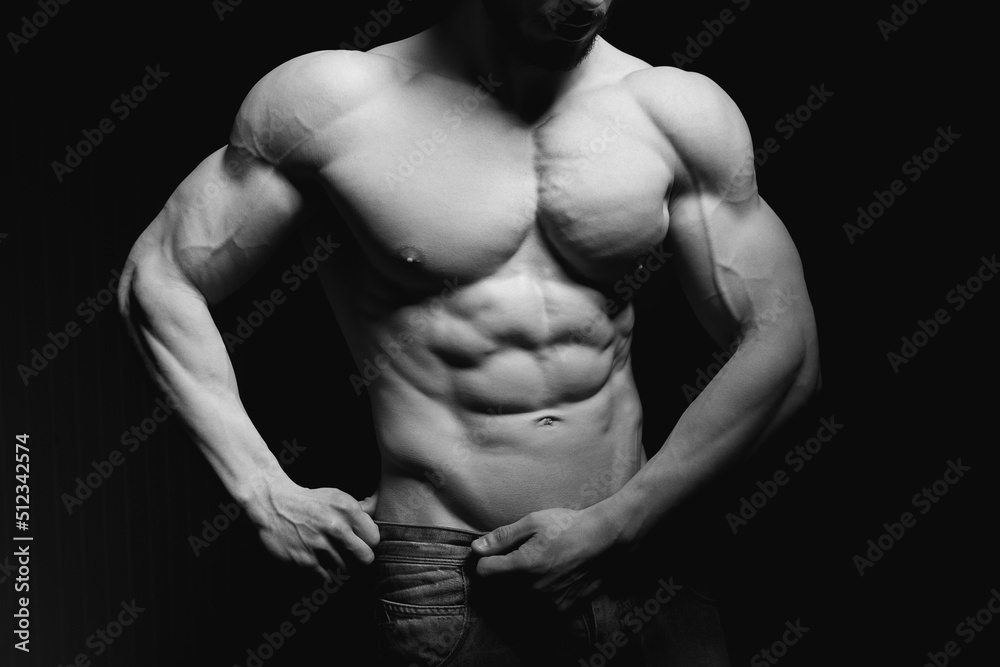 Portrait of shirtless muscular man in a jeans. Young male hunk showing his perfect body and muscles on black background Portrait of shirtless muscular man in a jeans. Young male hunk showing his perfect body and muscles on black background