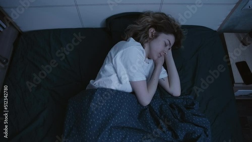 A young woman lies on her side in bed at night with her eyes closed, then checks the time on her phone, drinks water and closes her eyes again. Slow motion 4k footage