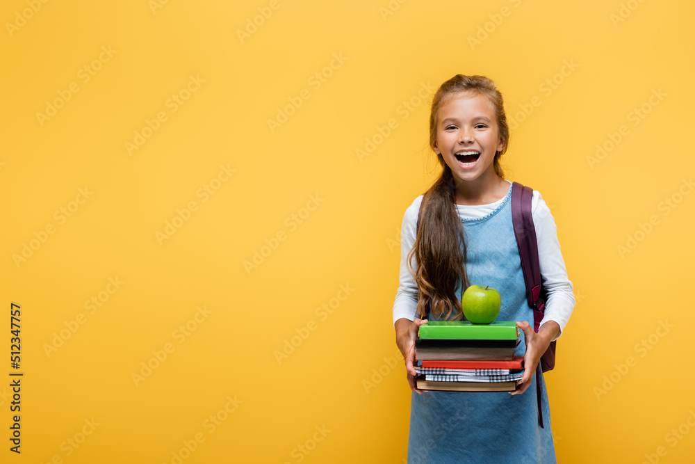 Cheerful pupil holding books and apple isolated on yellow. Cheerful pupil holding books and apple isolated on yellow.