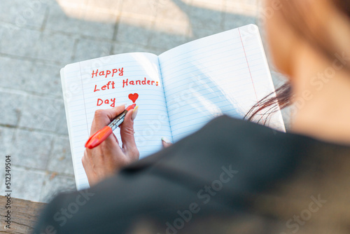 Woman writes in a notebook, holds felt-tip pen in her left hand.Outdoors summer evening park. Left-handers Day August 13th.Closeup. photo