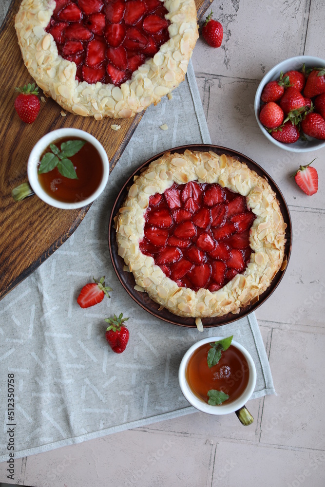 Delicious summer galette with pieces of juicy strawberries. Flat lay with open pies and cups of tea. Summer lunch with berry pastries. Delicious summer galette with pieces of juicy strawberries. Flat lay with open pies and cups of tea. Summer lunch with berry pastries.