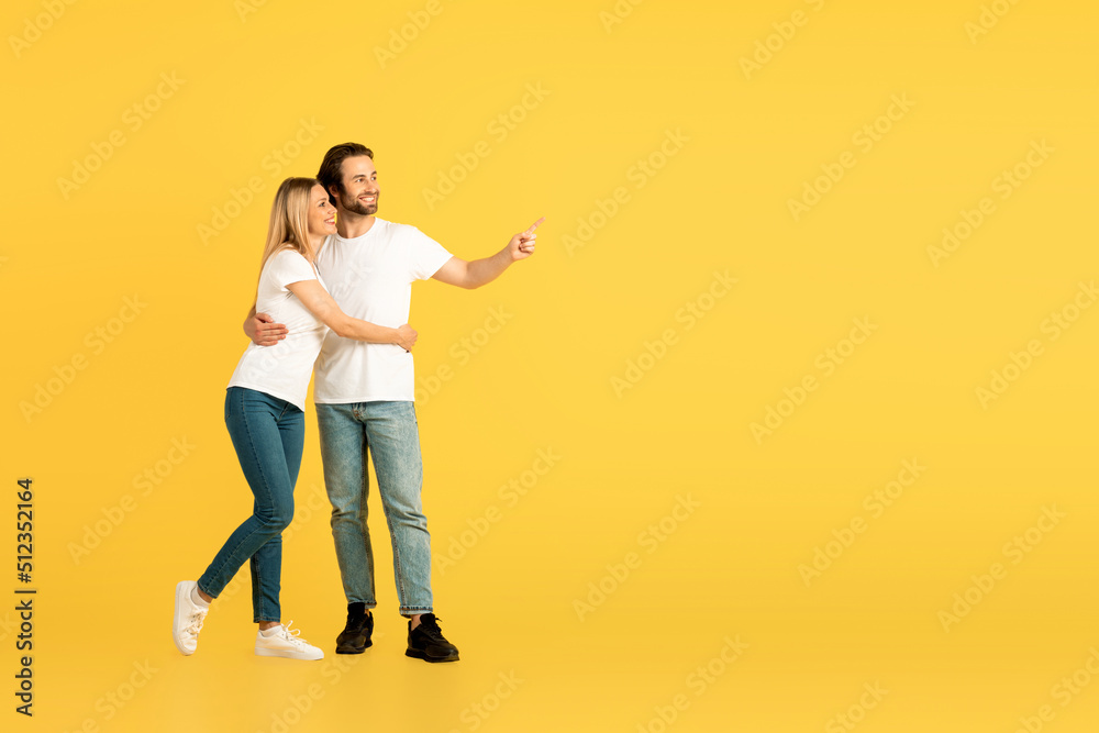 Glad happy millennial caucasian man and lady in white t-shirts hugging and pointing finger at empty space Glad happy millennial caucasian man and lady in white t-shirts hugging and pointing finger at empty space