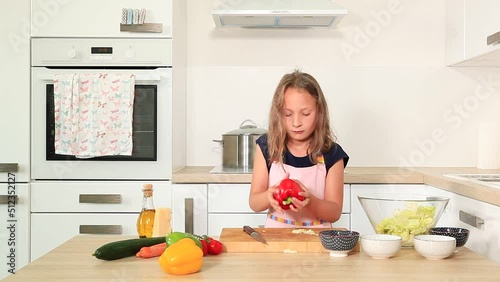 Cute girl cutting red pepper in modern kitchen.