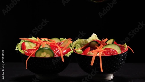 Olive oil puring on fresh vegetable salad on black background.
