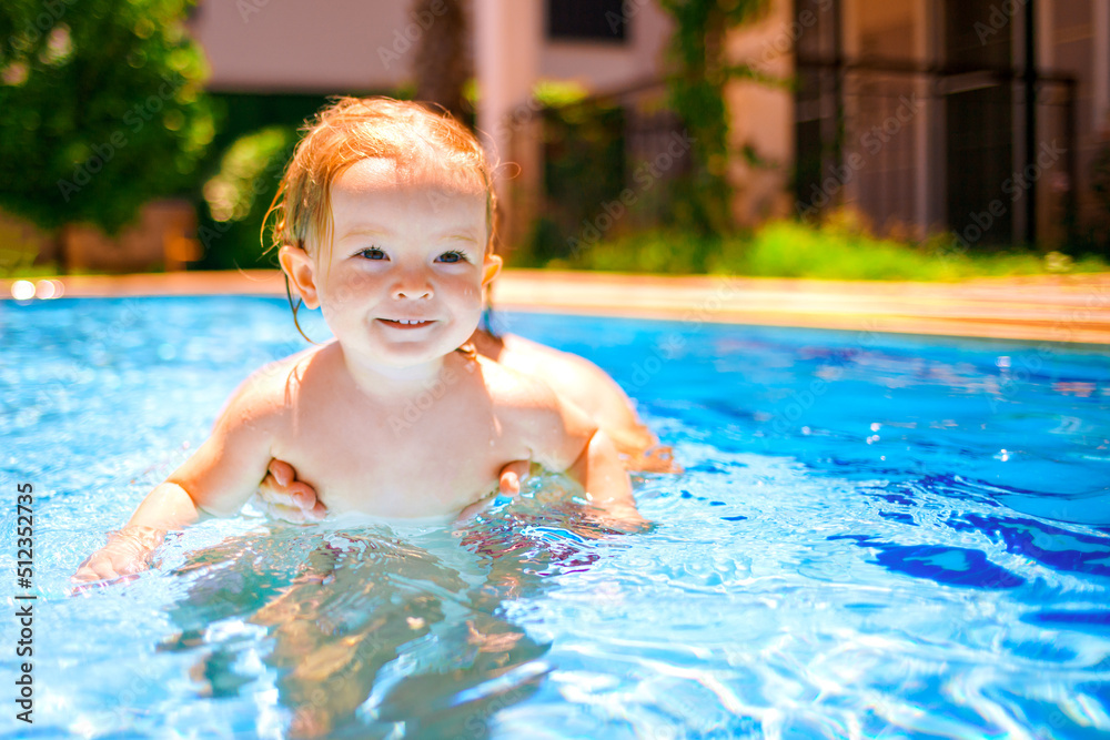 Little beautiful girl is splashing in the pool. Family happiness. The baby is learning to swim. The child has fun outdoors in the pool in the villa