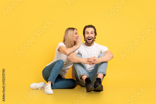 Cheerful millennial caucasian lady whispering to ear to shocked man in white t-shirt with open mouth