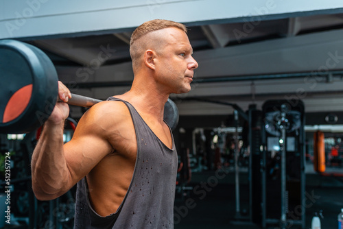 Fit young caucasian man lifting barbell, focused on weight, working out in a gym.Side view,copy space.