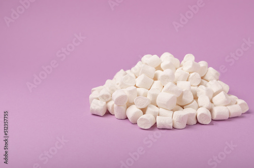 Loose marshmallows on a lilac background. White marshmallow flat lay. Sweets and snacks for a snack. Chewing candies close-up. Copy space. Place for text. Winter food concept.