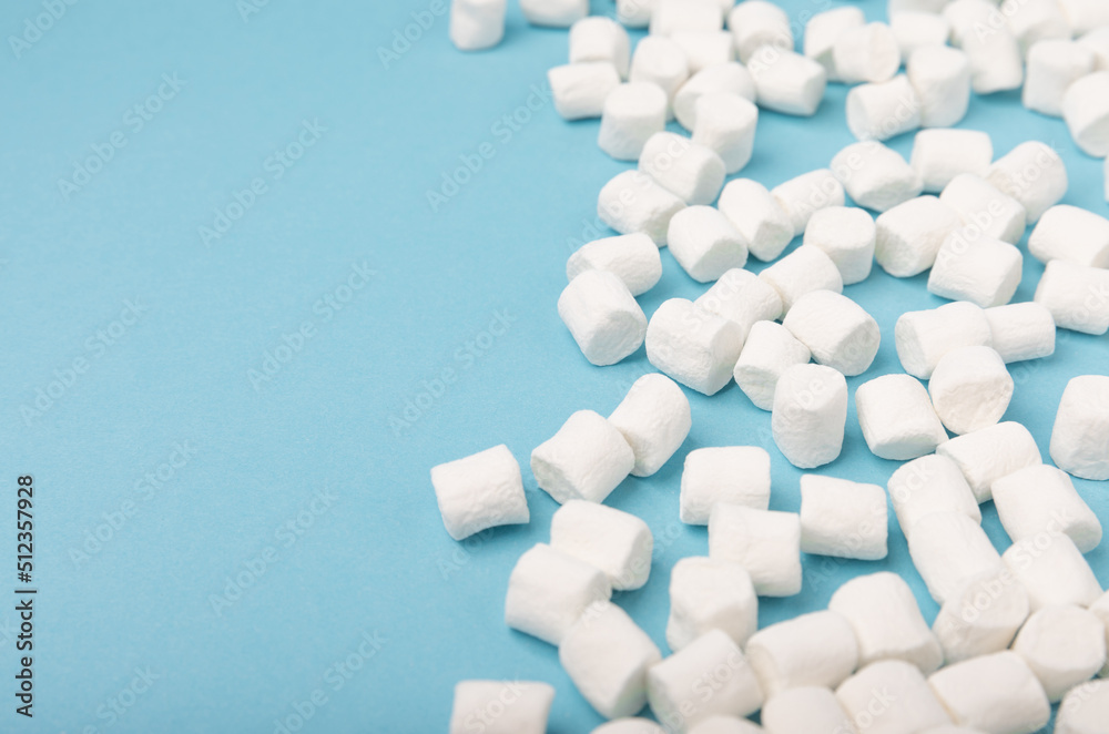 Loose marshmallows on a blue background. White marshmallow flat lay. Sweets and snacks for a snack. Chewing candies close-up. Copy space. Place for text. Winter food concept. Loose marshmallows on a blue background. White marshmallow flat lay. Sweets and snacks for a snack. Chewing candies close-up. Copy space. Place for text. Winter food concept.
