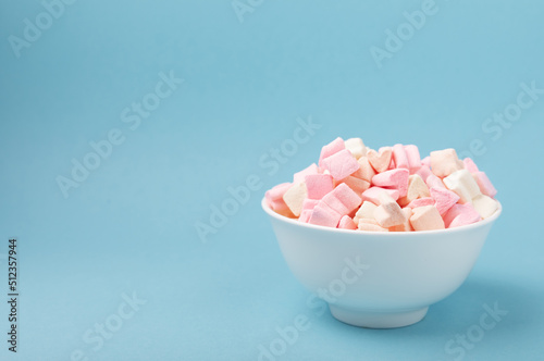 Marshmallows in plates on a blue background.Close-up strawberry flavored chewy candy.Snacks and snacks for parties.Spice for coffee and cocoa.Winter food concept.Place for text.