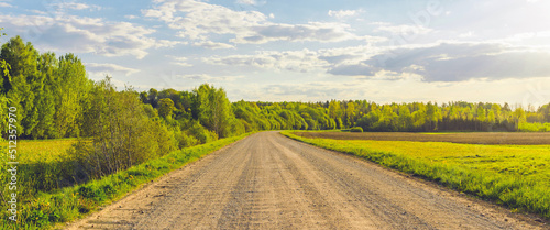 Empty Sandy country road near the forest,fluffy clouds blue sky,summer evening landscape.Banner.