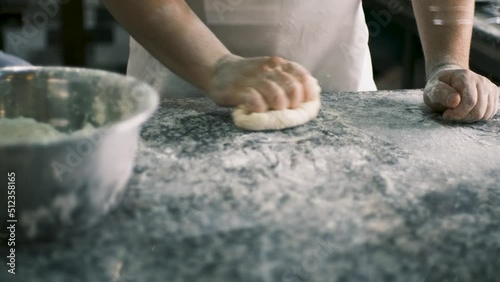 A chef kneads dough from pizza flour with his hands and forms a cake. View from behind the glass. 