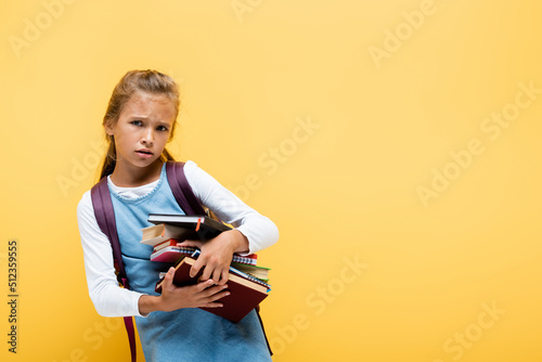 Sad schoolkid holding books and notebooks isolated on yellow.