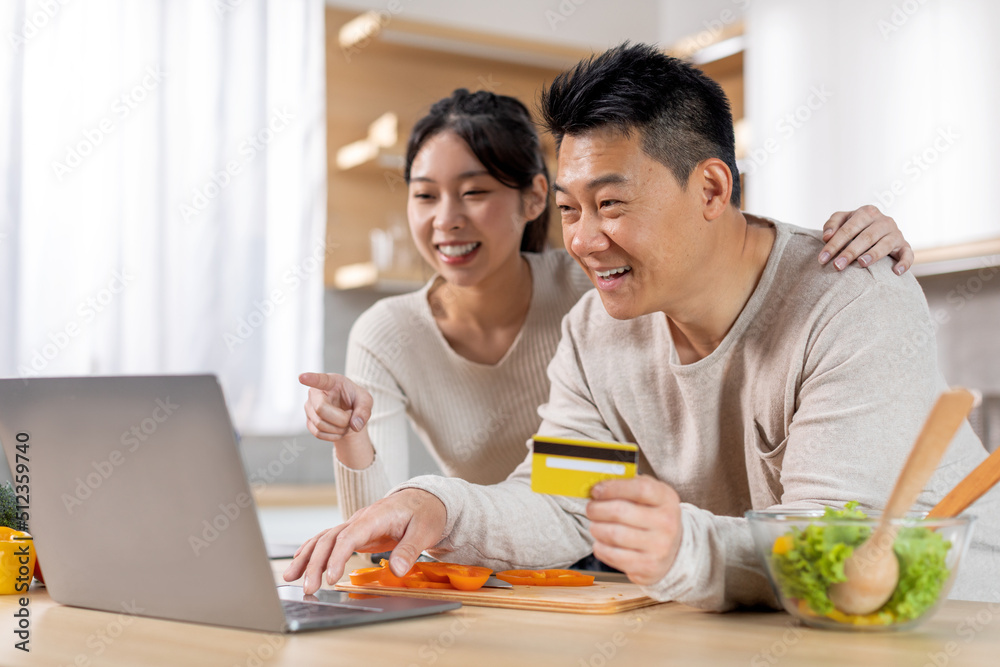 Excited asian couple making online order, using laptop at kitchen