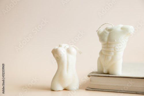 Close up of two handmade candles from soy wax in shape man torso and woman body isolated on pastel beige background.