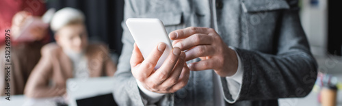 partial view of man using mobile phone in ad agency on blurred background, banner.