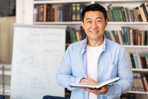 Korean Male Teacher Holding Book Standing Near Whiteboard In Classroom