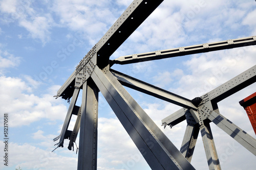 A war-torn railroad bridge truss against the sky.