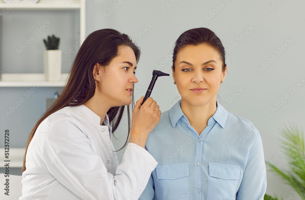 Diagnosis and treatment of diseases of ear. ENT doctor uses otoscope to examine female patient's ear during medical examination at hospital. Female otolaryngologist consults in her office. Diagnosis and treatment of diseases of ear. ENT doctor uses otoscope to examine female patient's ear during medical examination at hospital. Female otolaryngologist consults in her office.
