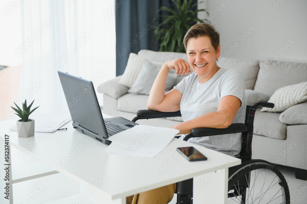 Freelancer in wheelchair using laptop near notebook and papers on table Freelancer in wheelchair using laptop near notebook and papers on table