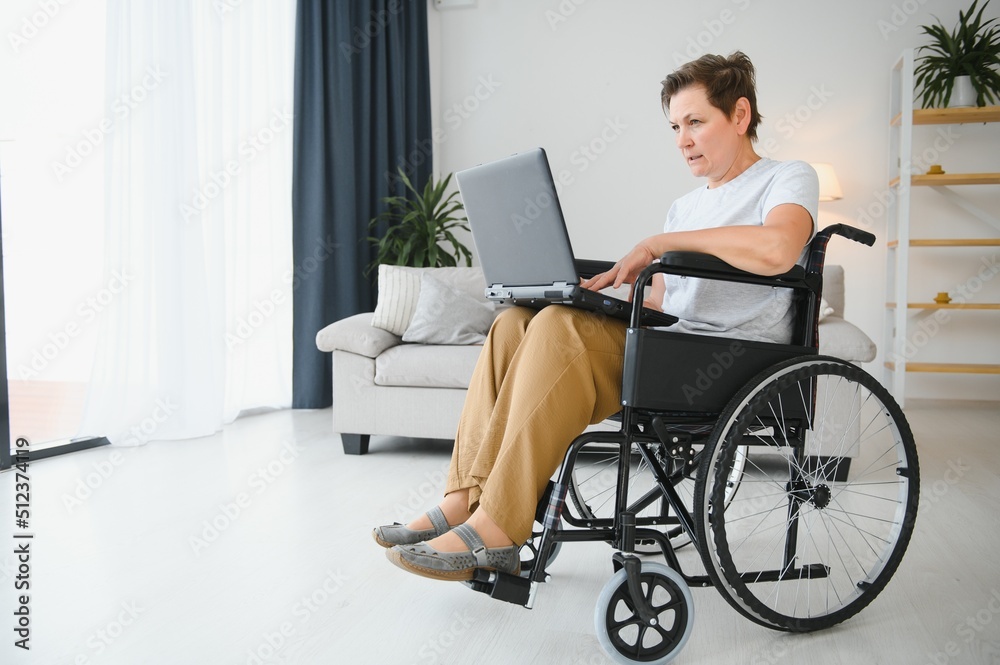 Middle age woman using laptop sitting on wheelchair at home