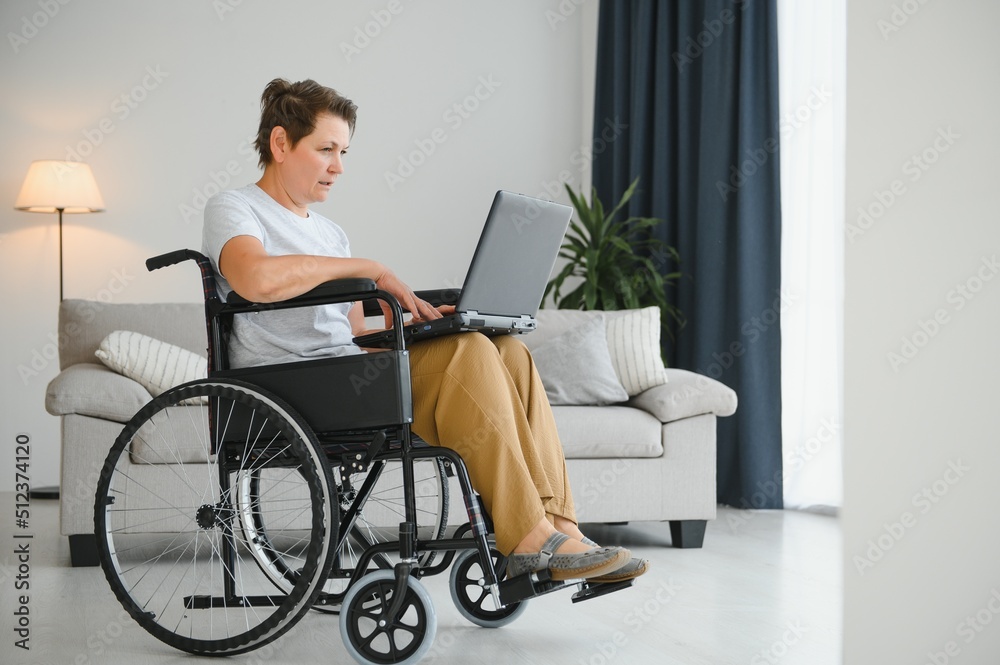 Middle age woman using laptop sitting on wheelchair at home Middle age woman using laptop sitting on wheelchair at home
