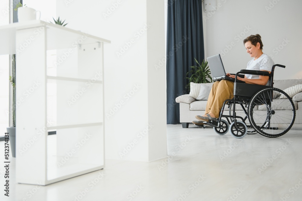 Fototapeta premium Middle age woman using laptop sitting on wheelchair at home