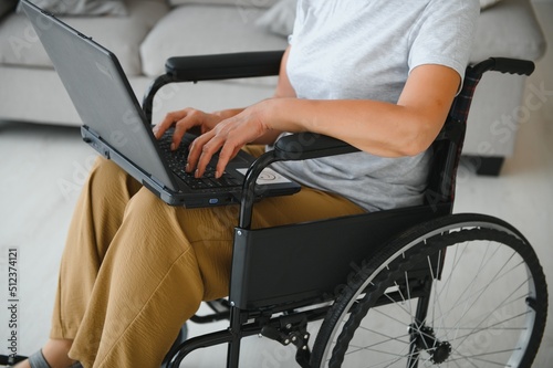 Positive elderly woman in wheelchair working on laptop, IT freelancer, online