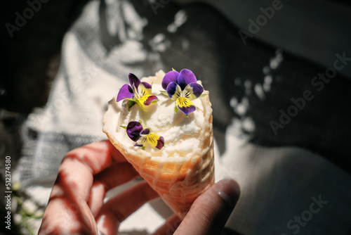 Hand holding an ice cream decorated with pansies, contrast light, aesthetic summer mood