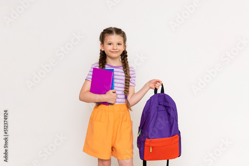 A schoolgirl with books holds a backpack in her hand on a white isolated background. Preparation for the academic year.
