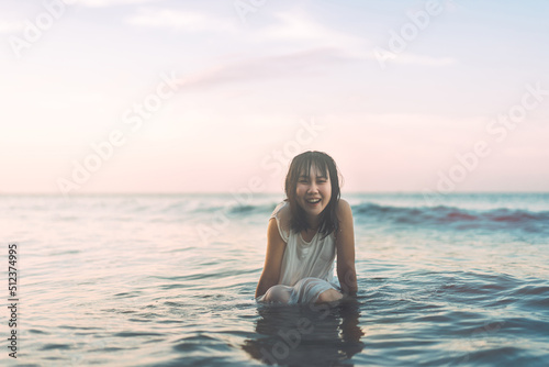 Portrait of asian woman at the beach sitting in the sea waves sunlight background.