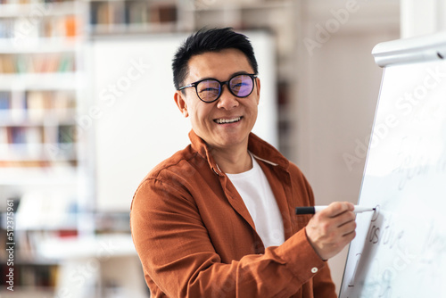 Positive Asian Teacher Man Smiling Writing On Whiteboard In Classroom photo