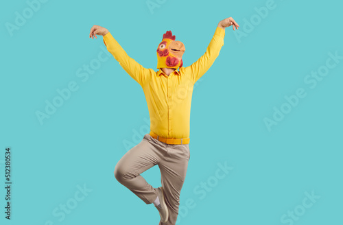Canvastavla Cheerful young man in rubber rooster mask shows funny dance moves on turquoise background