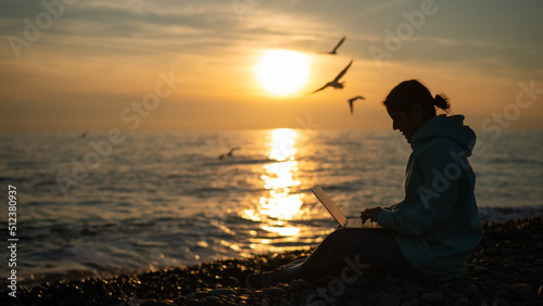 Caucasian woman typing on a laptop on the seashore at sunset. Freelance work.