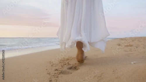Cinematic summer vacation on beautiful tropical beach in slow motion on RED camera. Woman is elegant white waving dress walking barefoot by clear sandy golden beach. Sunset cloudy sky on background 6K