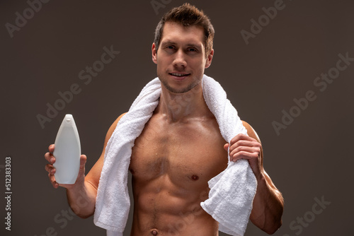 Portrait of attractive man with perfect body preparing to applying shampoo at his hair isolated on brown background. Self care concept