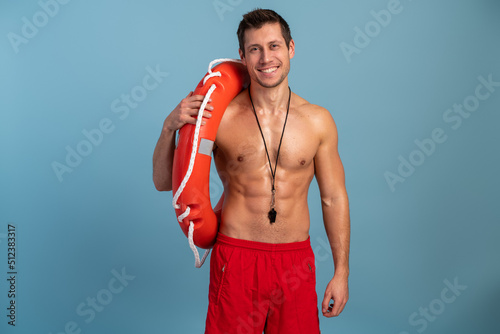 Waist up photo of nice brunet young guy holding buoy and looking at the camera shorts isolated on blue color background