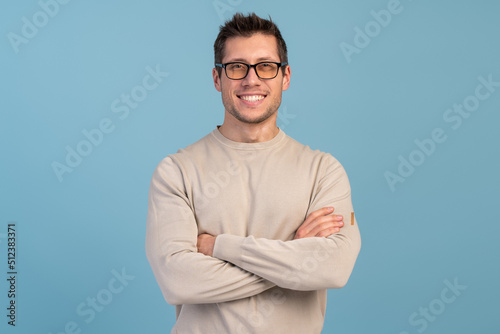 Portrait of young smiling caucasian man with crossed arms, wearing casual closes posing isolated on blue background