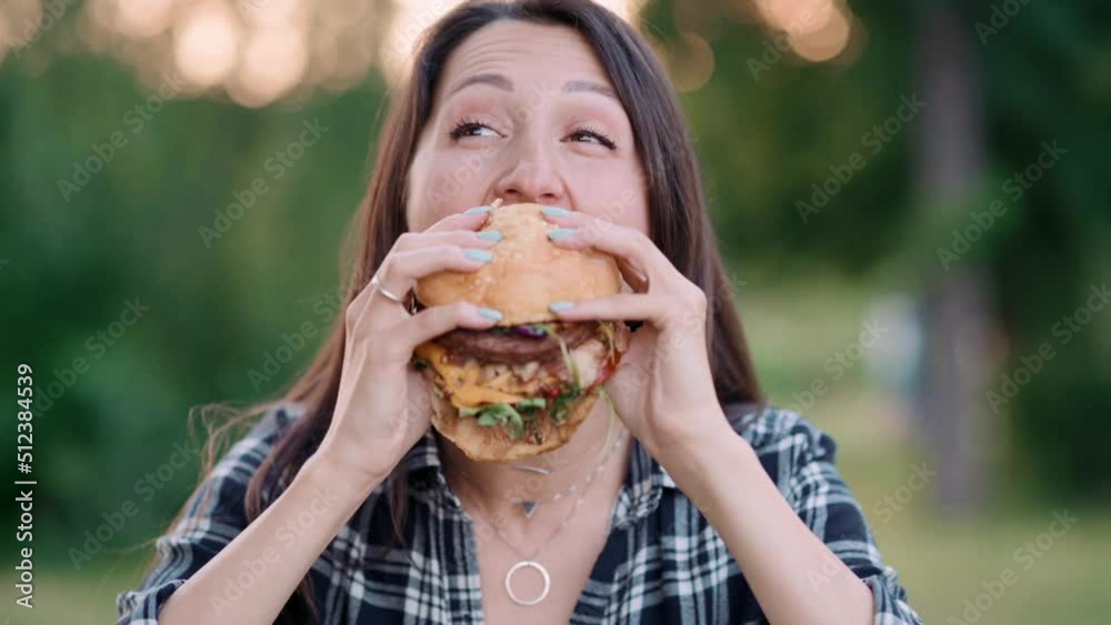 Young attractive hungry woman bites a big hamburger outdoor. Close up.