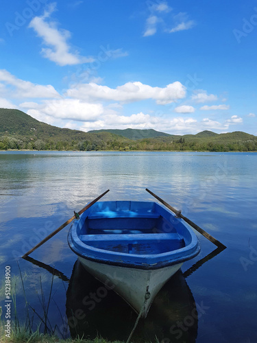 Fotografie, Obraz Small rowing wooden boat, with oars on lake with calm water and green hills under blue sky with autumn clouds